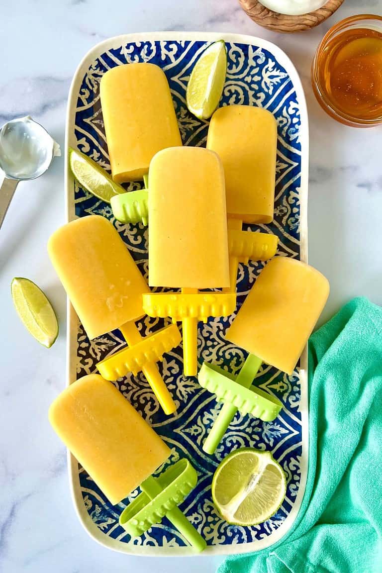 Mango freezer pops on a blue and white patterned platter with lime wedges.