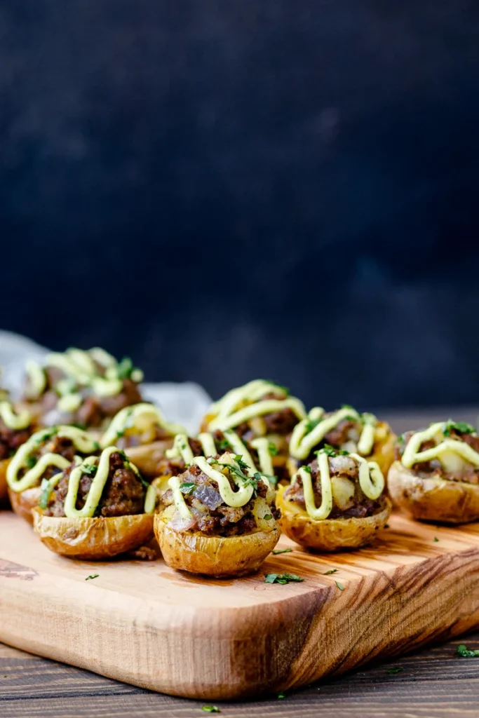 Mini halved potatoes topped with ground beef and a creamy sauce drizzled on top.