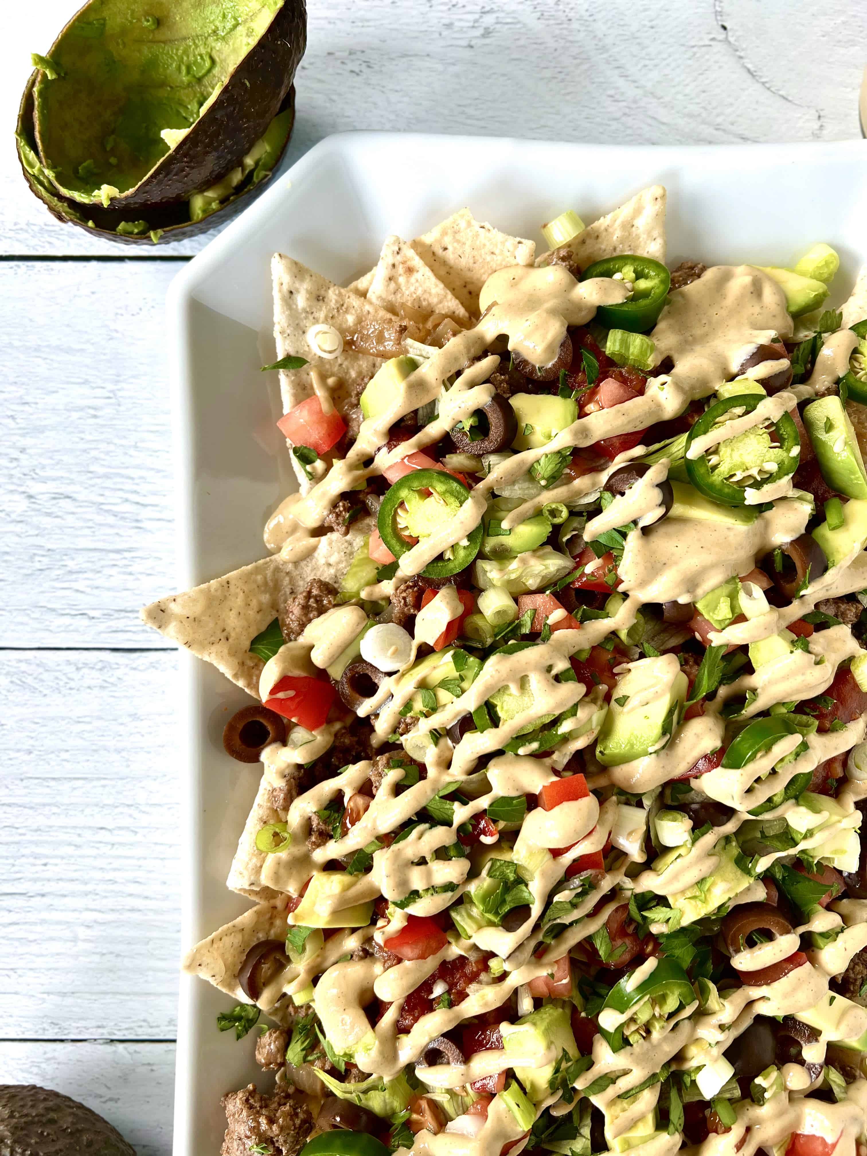 Grain-free nachos with all the toppings and a dairy-free nacho cheese sauce on a white platter.