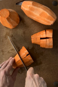 Slicing peeled sweet potatoes on a cutting board.