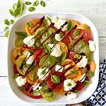 An Italian caprese salad with burrata cheese and fresh basil leaves in a white platter.