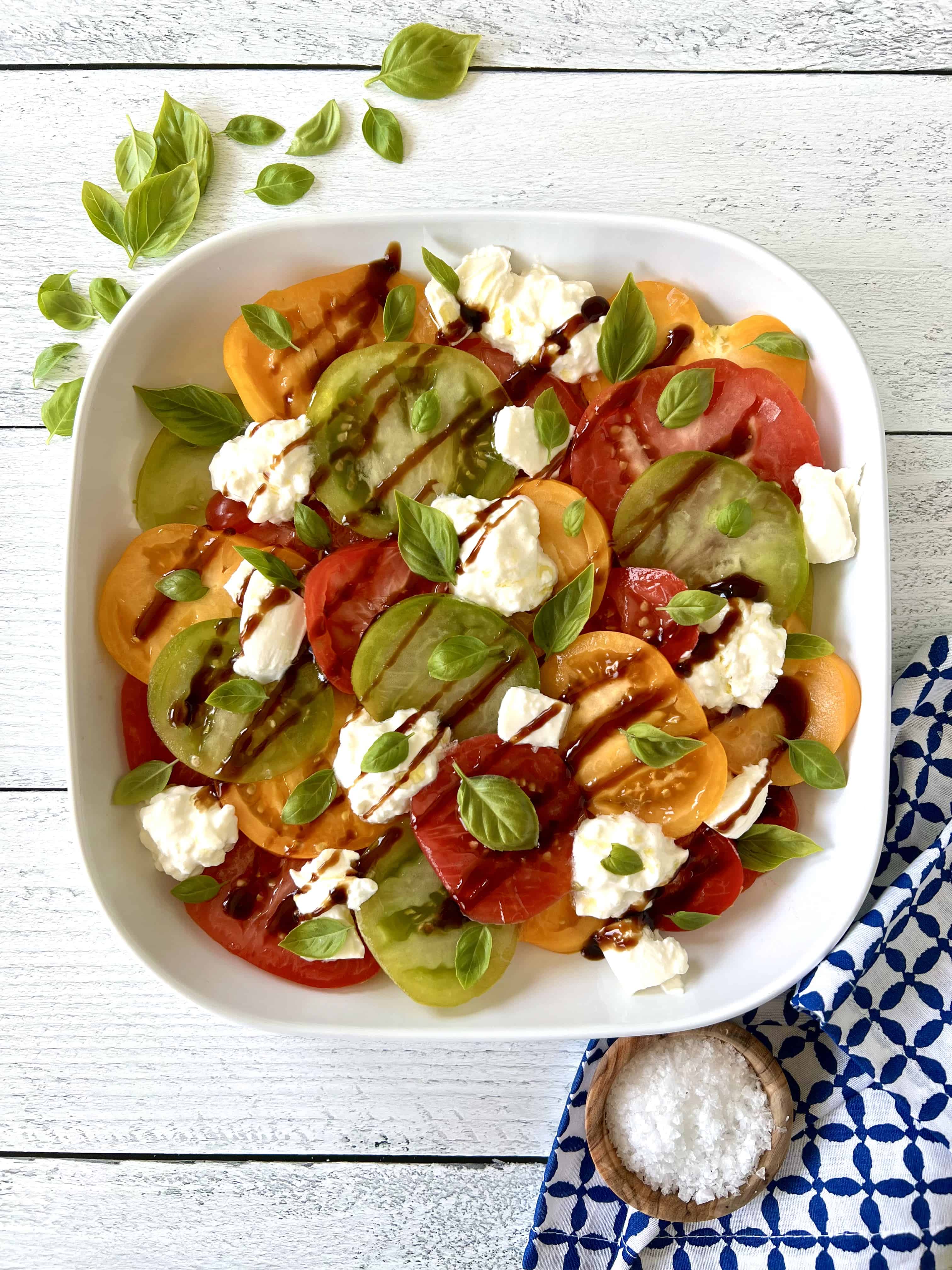 An Italian caprese salad with burrata cheese and fresh basil leaves in a white platter.