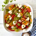 A tomato salad with burrata cheese and basil leaves in a white platter.