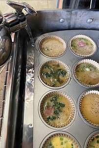A muffin pan full of egg cups in a metal roasting pan with a tea kettle pouring hot water into the roasting pan.