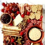 A Charcuterie Board with cheeses, meats, glute-free crackers, olives, nuts, fruit, dried fruit and cornichon on a wooden cutting board on a marble table.