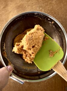 Almond flour cookie dough on a spatula over a metal bowl with more dough.