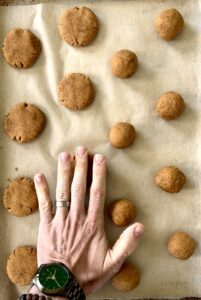 A hand flattening cookies on a parchment-lined baking sheet.