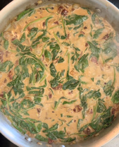 A creamy sun-dried tomato spinach sauce in a pan.