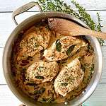 Healthy Tuscan Chicken in a stainless steel skillet with a wooden spatula and a green napkin wrapped around its handle, next to a bunch of thyme sprigs.