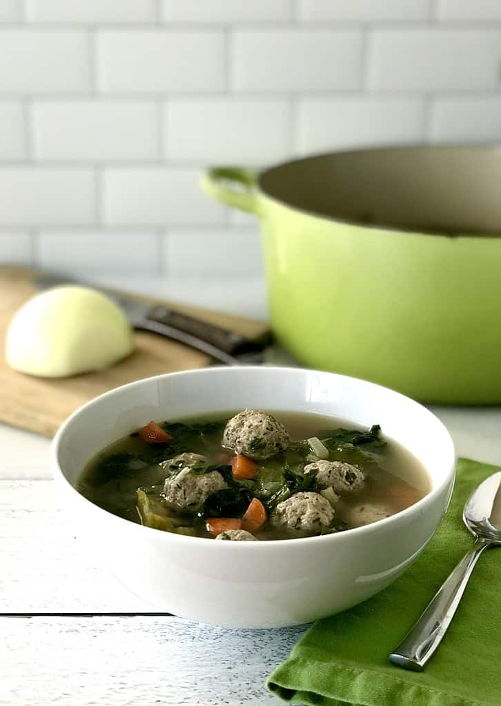 Low carb Italian Wedding Soup in a white bowl next to a green napkin with a spoon on it.