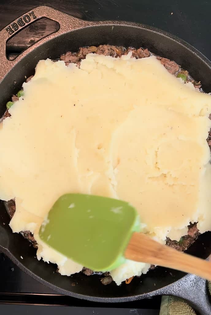 Smoothing mashed potatoes over ground beef in a cast iron skillet.