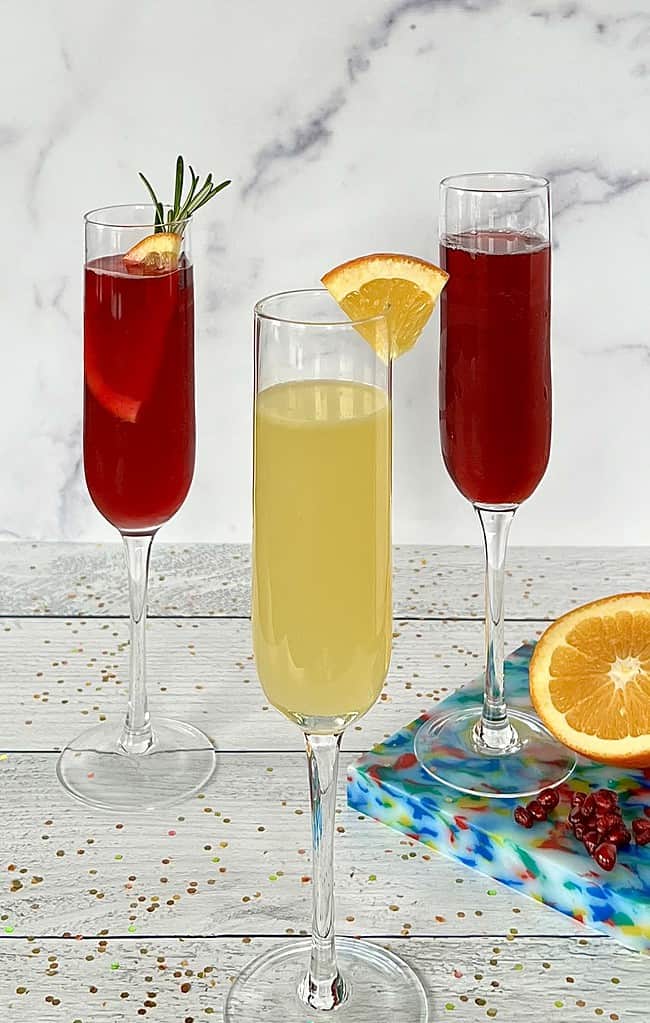 Three alcohol free mimosas in champagne flutes on a white table covered in glitter.