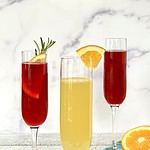 Three non alcoholic mimosas in champagne flutes on a white table covered in glitter.