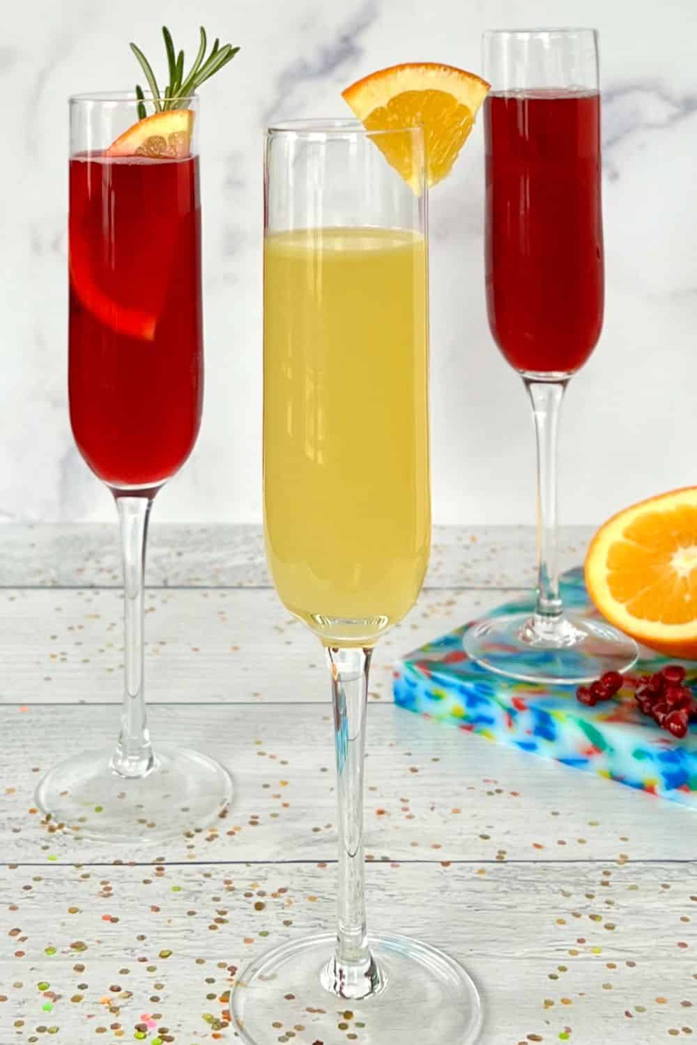Three healthy mocktails in champagne flutes on a white table covered in glitter.