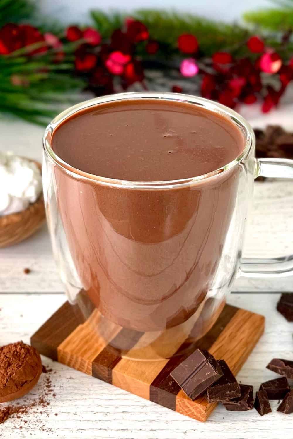 Healthy hot chocolate in a glass mug surrounded by garland, cocoa powder and chopped chocolate.