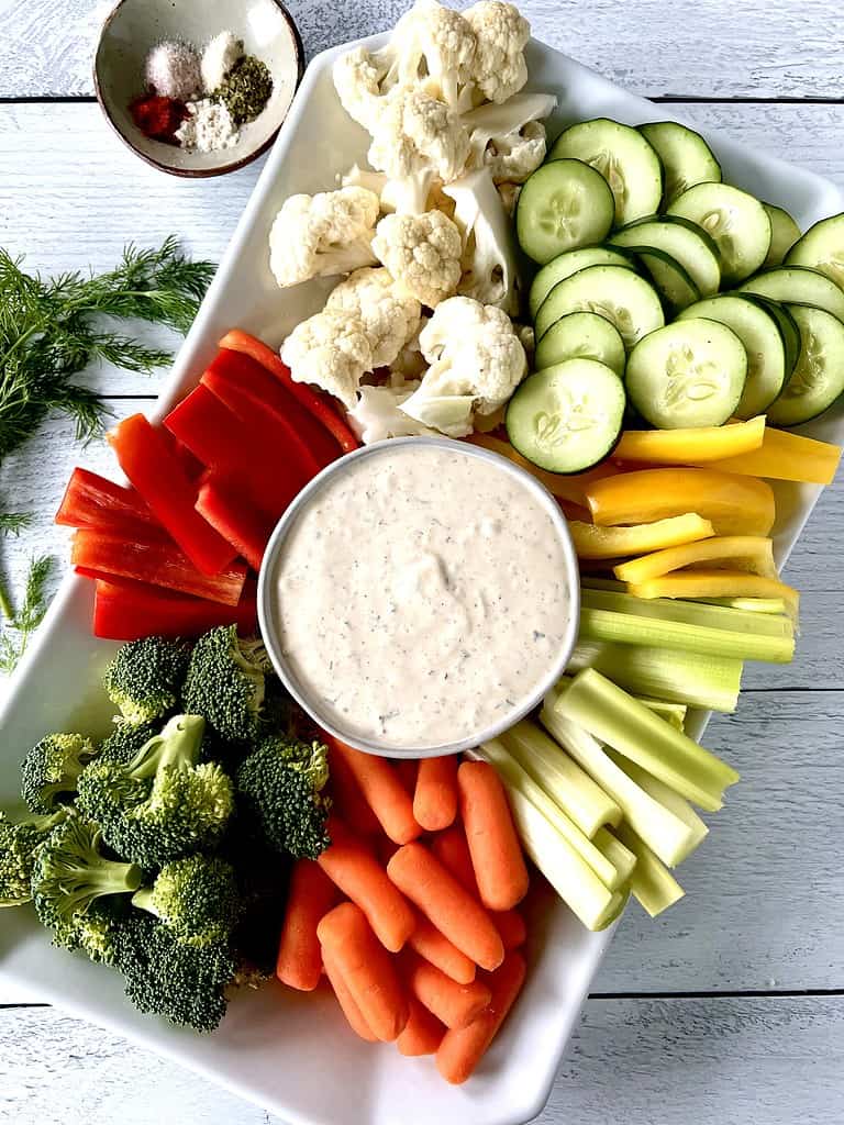 Paleo veggie dip in a white bowl surrounded by carrots, cucumber, cauliflower, peppers, broccoli and celery.