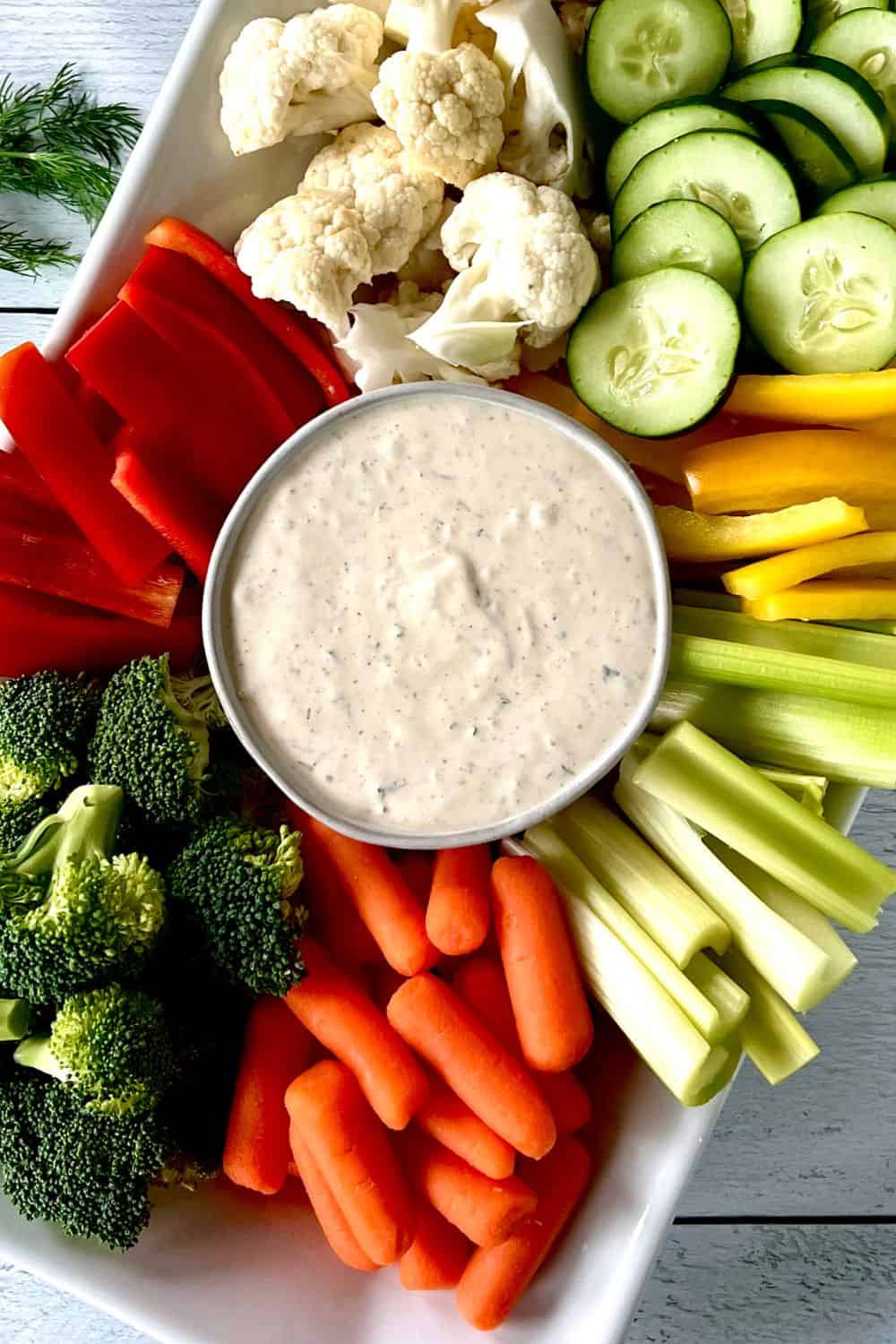 Non dairy veggie dip in a white bowl surrounded by carrots, cucumbers, peppers, broccoli and peppers.