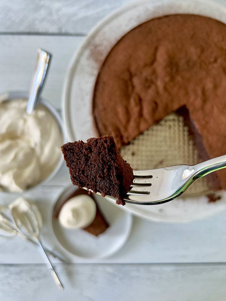A fork holding up a bite of flourless espresso chocolate cake over the cake and a slice of the cake.