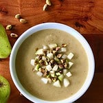 Easy Parsnip Soup in a white bowl on a wooden table surrounded by pears and pistachios.