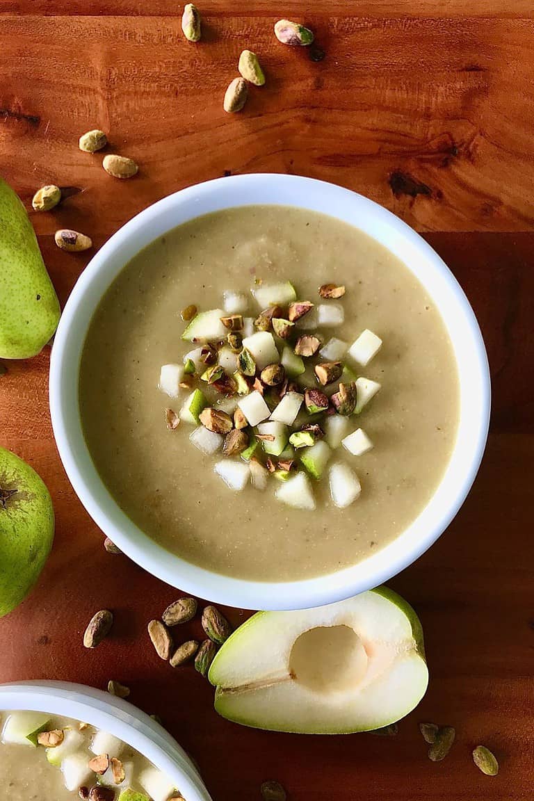 Easy Parsnip Soup in a white bowl on a wooden table surrounded by pears and pistachios.