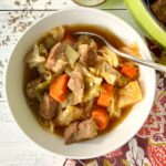 Cabbage and pork stew in a white bowl next to a small bowl of caraway seeds.