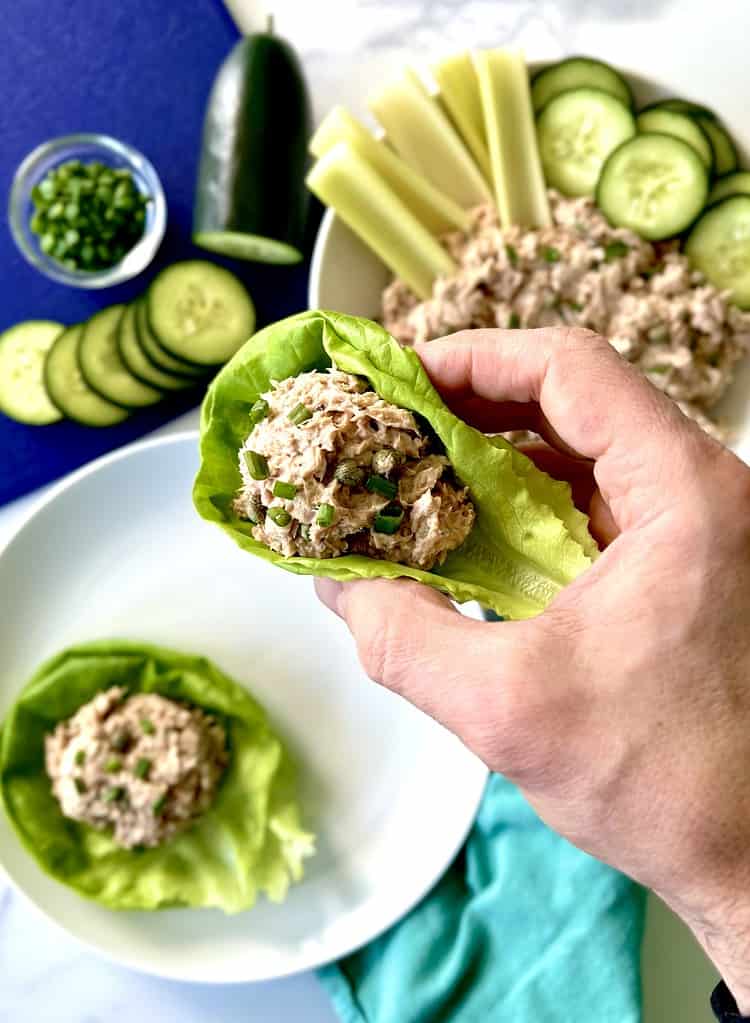 A hand holding up a lettuce cup with tuna salad scooped inside.