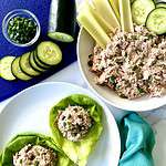 Low carb tuna salad scooped into lettuce cups on a plate and in a bowl with celery sticks and cucumber slices.