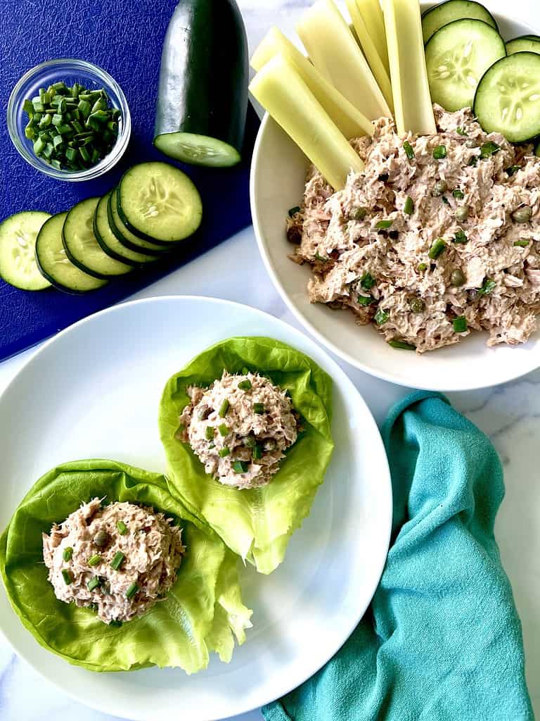 Low carb tuna salad scooped into lettuce cups on a plate and in a bowl with celery sticks and cucumber slices.