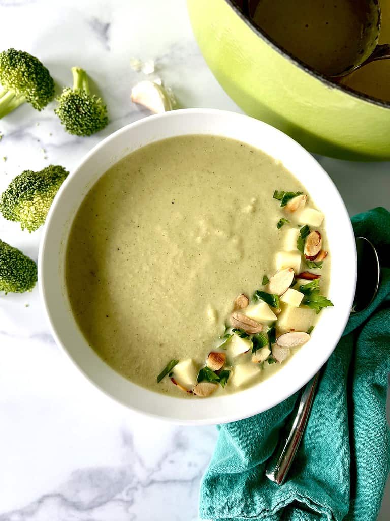 Healthy broccoli soup in a bowl topped with parsley, diced apples and sliced almonds.