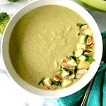Broccoli and almond soup in a bowl topped with sliced almonds, parsley and diced apples.