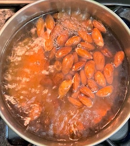 Boiling almonds in water in a saucepan.