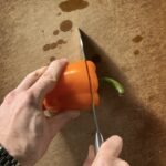 Cutting an orange bell pepper.