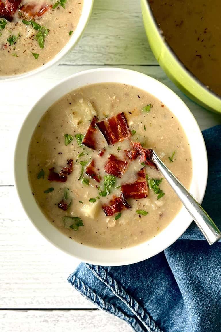 Gluten-free clam chowder in a white bowl topped with bacon.