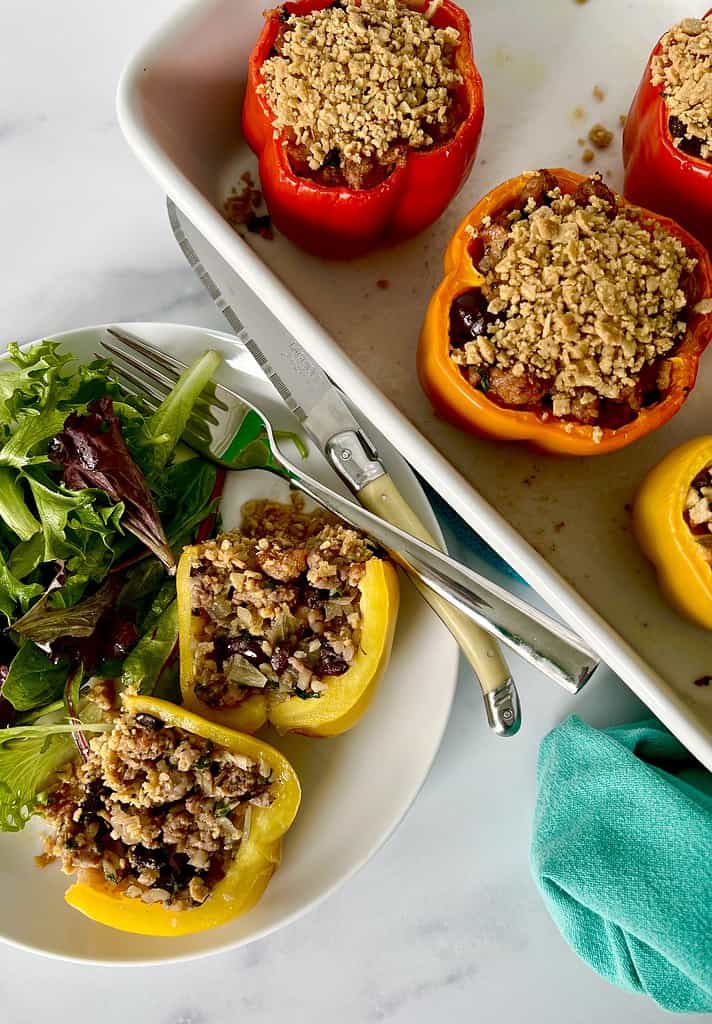 Low carb stuffed peppers sliced in half next to a salad on a white plate and whole stuffed peppers in a white baking dish.