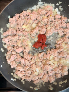 Sausage, diced onion and tomato paste in a skillet.