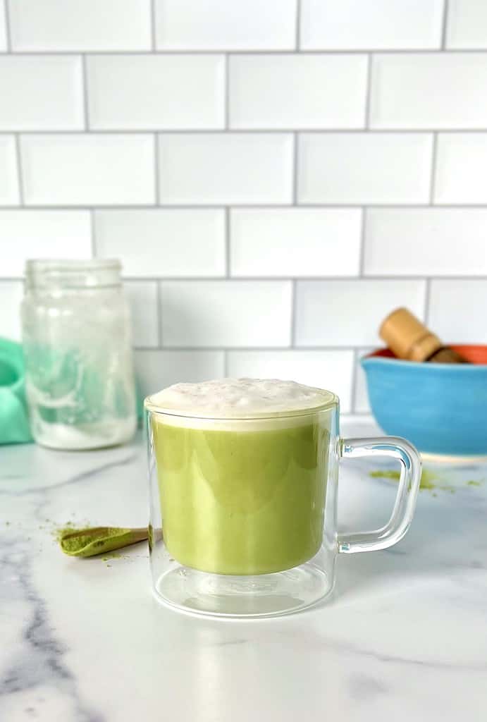 A healthy matcha latte in a glass mug on a marble table.