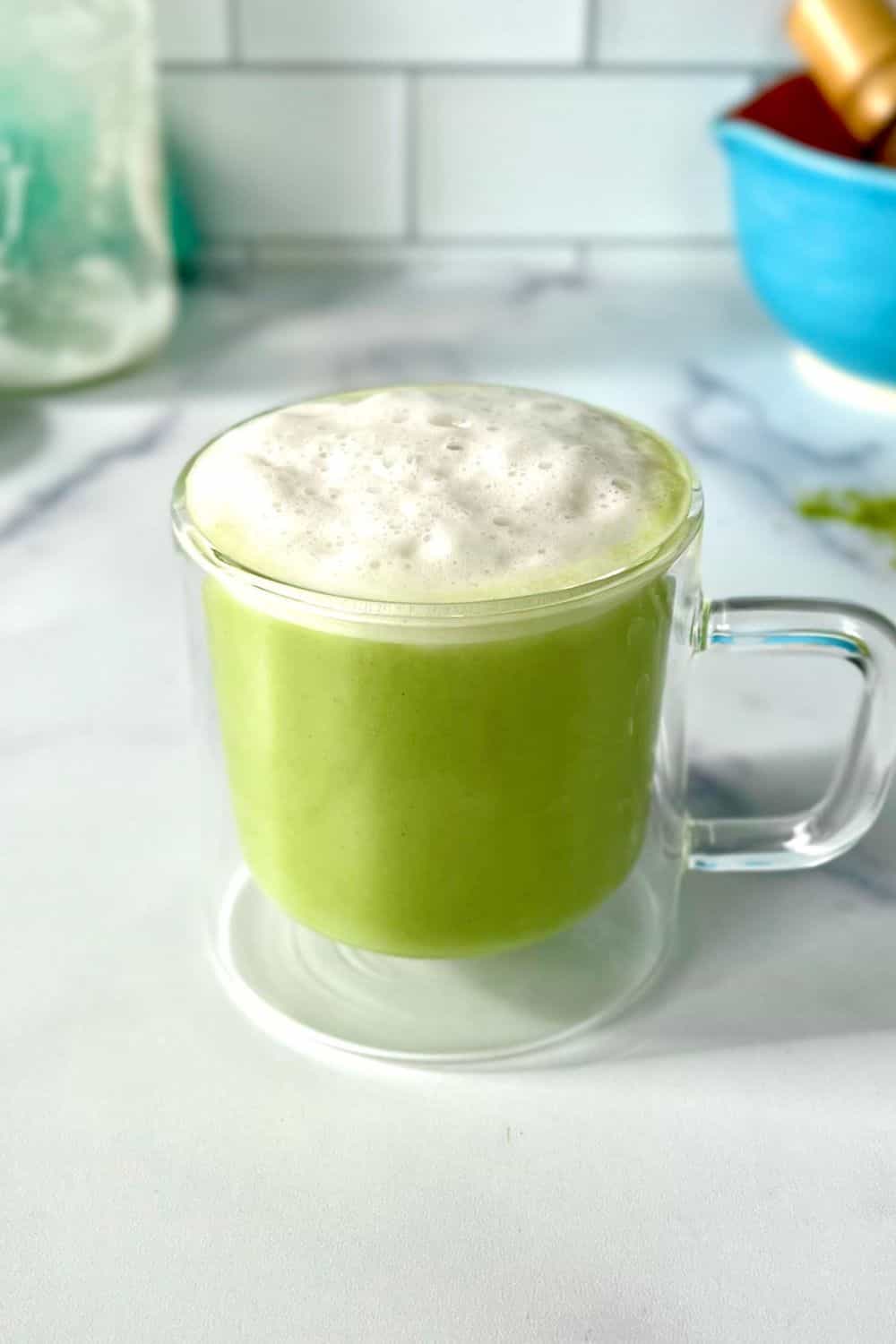 A matcha latte with almond milk in a glass mug.