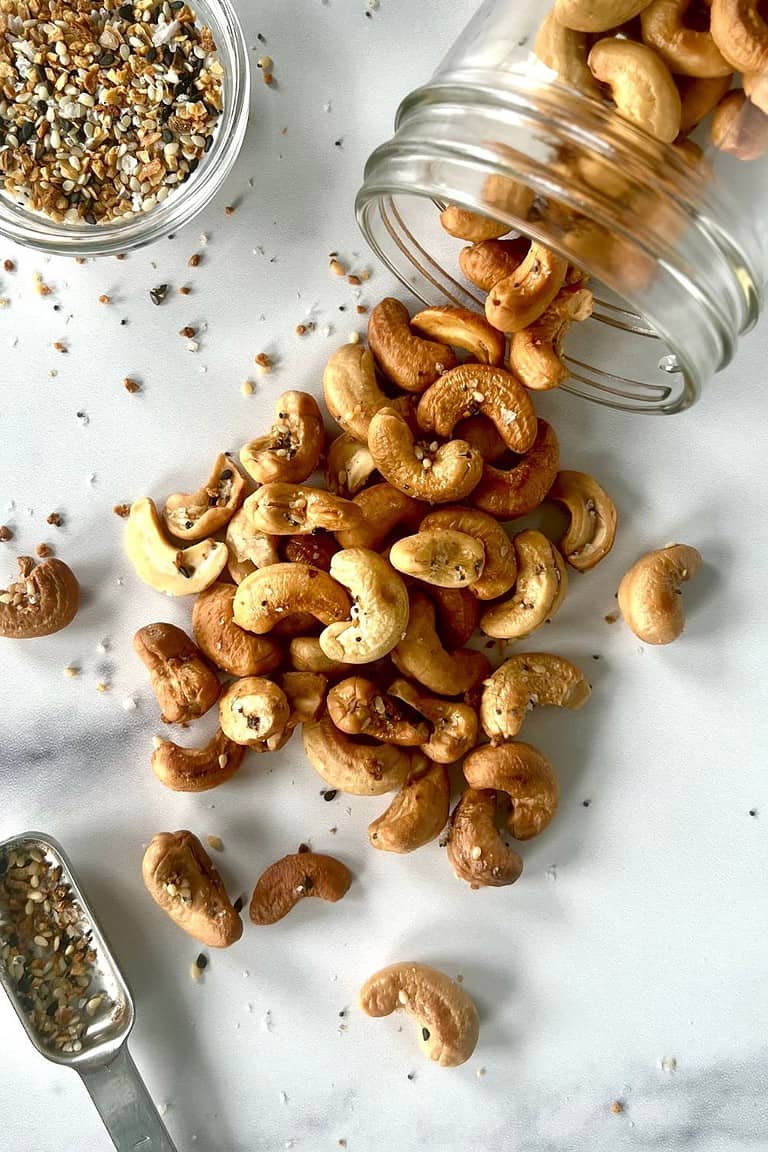 Roasted cashews spilling out of a glass jar onto a marble table.
