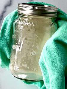 A hand wrapped in a towel holding a glass jar of milk.
