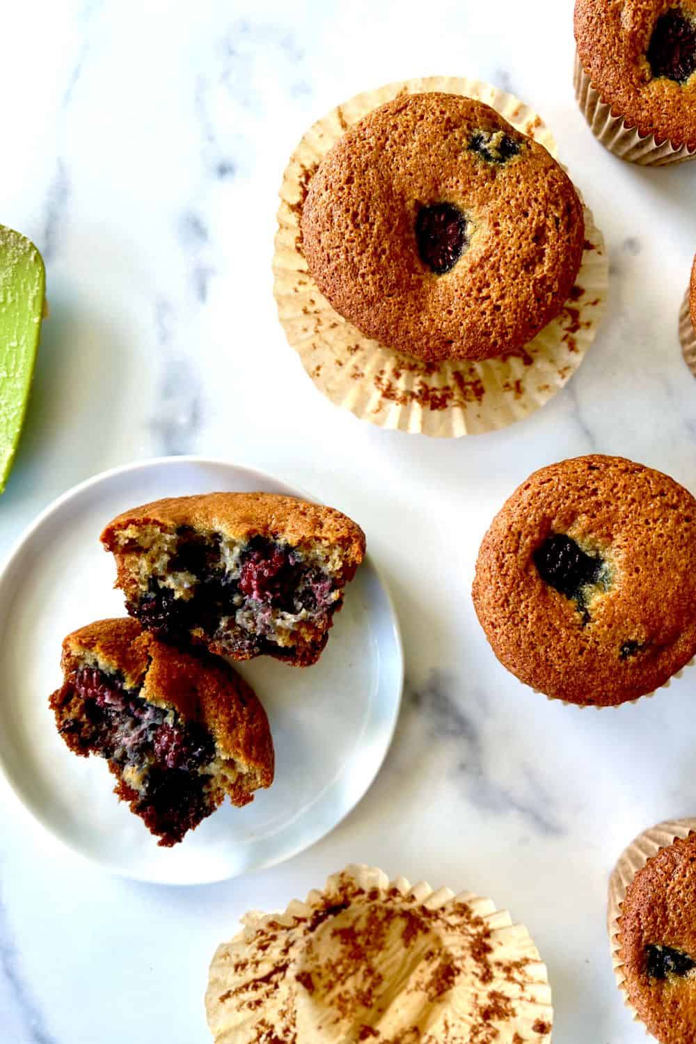 Paleo blackberry muffins on a marble table and one muffin split in half on a plate.