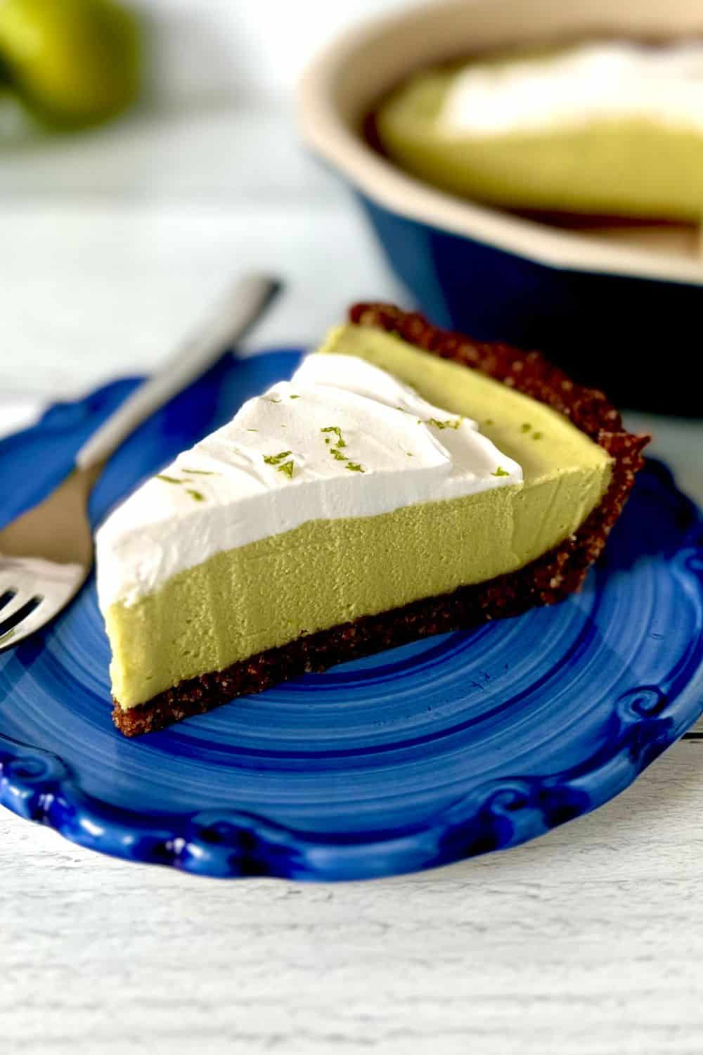 A slice of Paleo key lime pie on a blue plate with a fork.