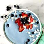A blue spirulina recipe for a smoothie bowl, topped with blueberries, strawberries and coconut flakes.