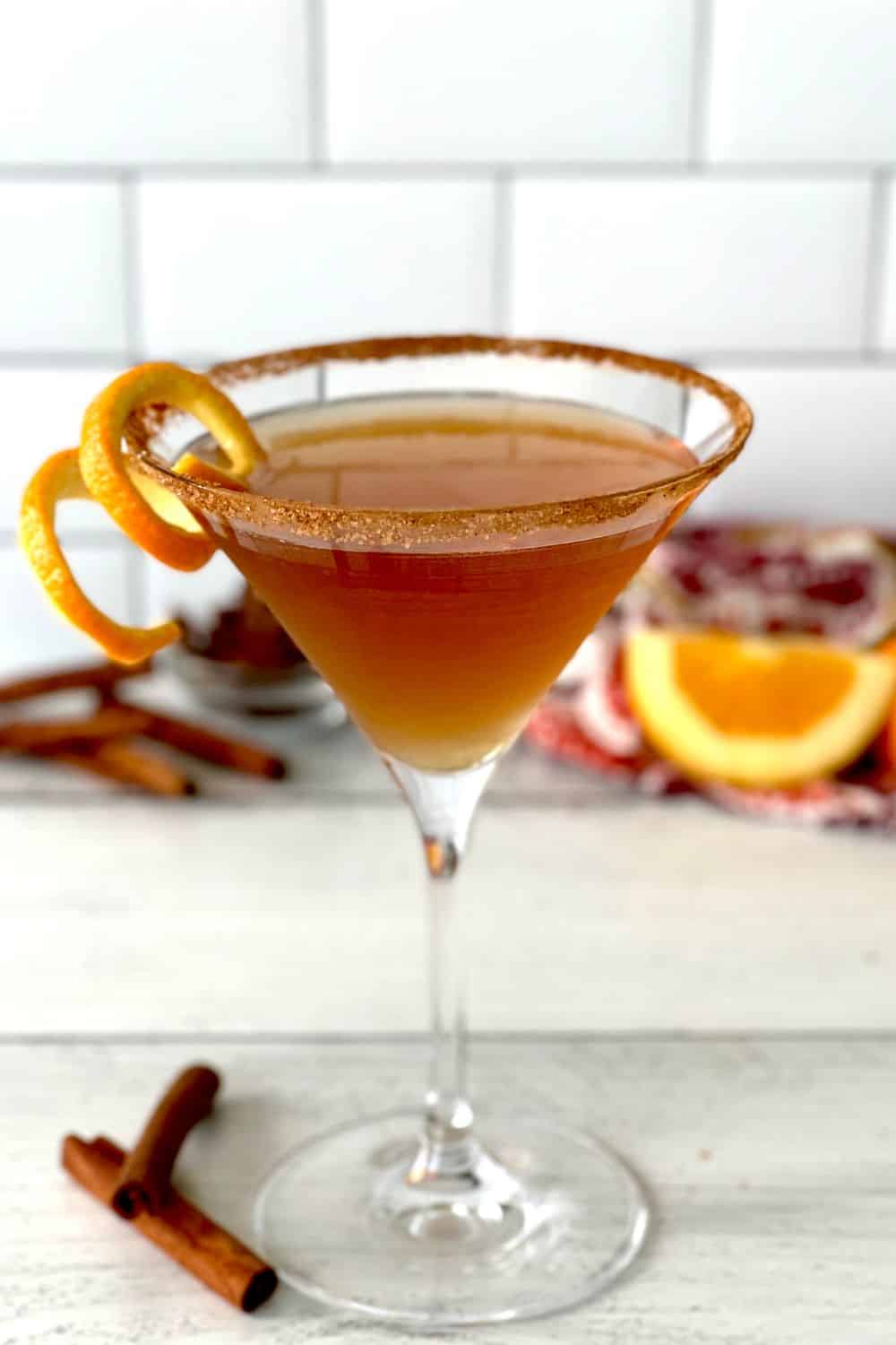 A chai tea martini in a martini glass garnished with an orange twist.