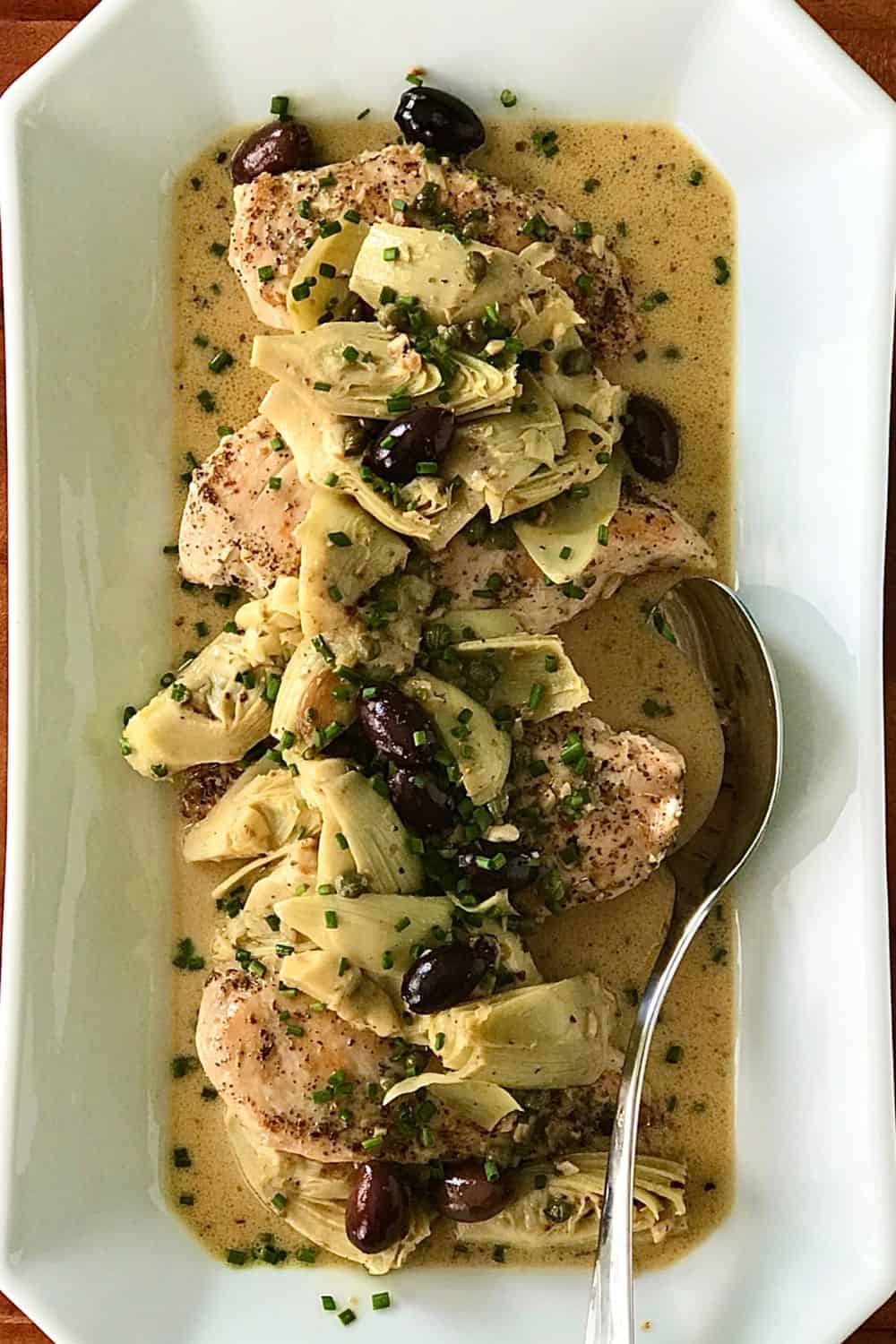 Creamy Lemon Chicken, Olives and Artichokes on a long platter with a serving spoon.