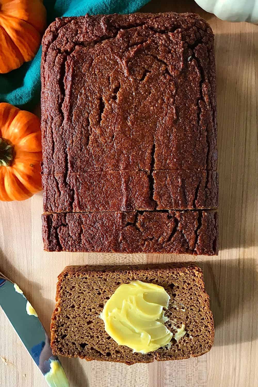 Coconut Flour Pumpkin Bread on a cutting board with a slice laying flat with a smear of butter on it.