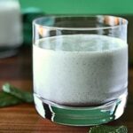 Dairy-free shamrock shake on a wooden table with fresh mint leaves around it.