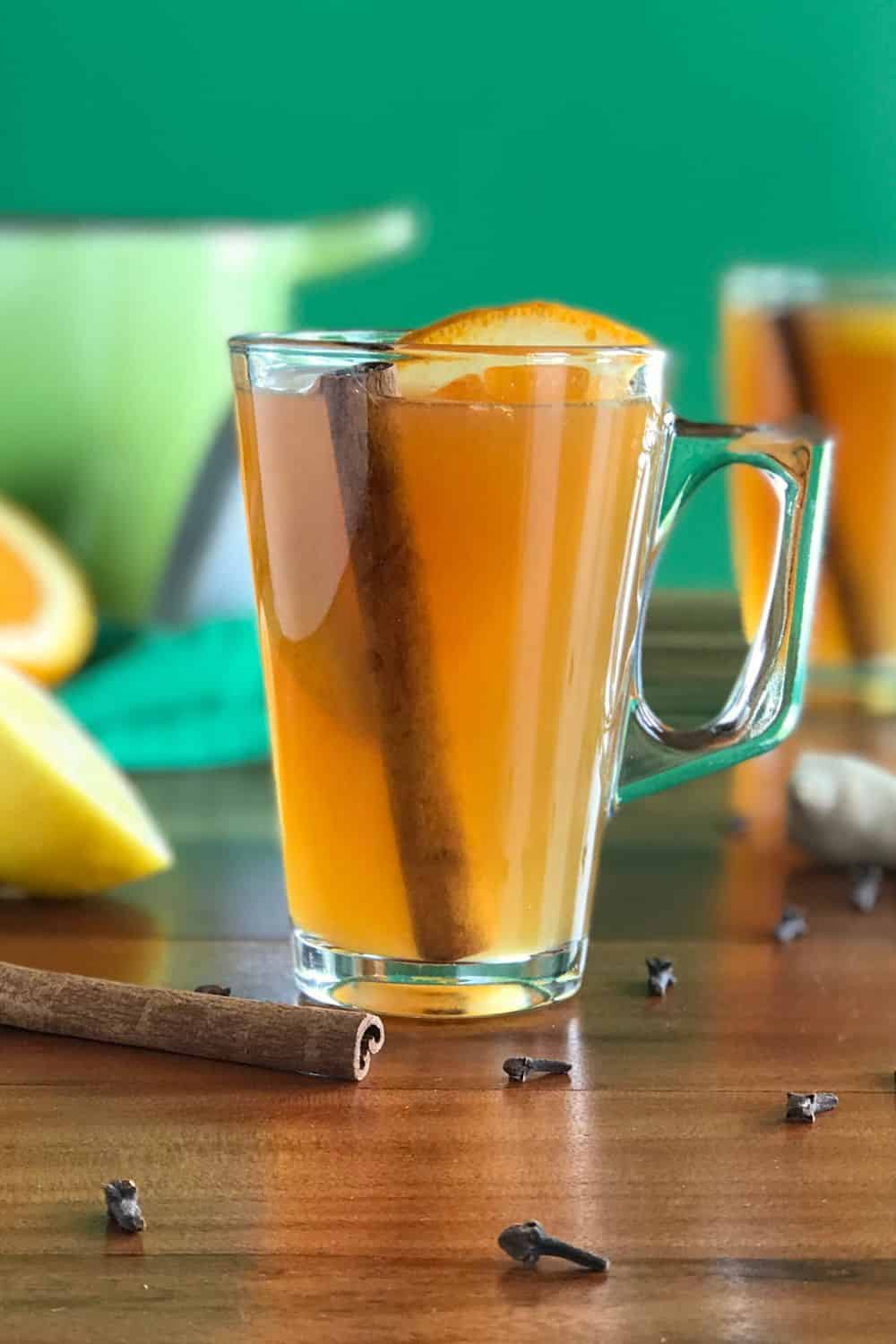 Mulled Apple Cider in a glass mug with an orange slice and cinnamon stick.