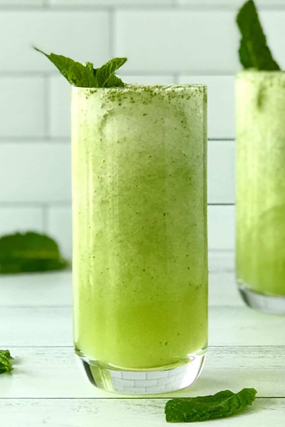 A tall glass with a honeydew mocktail topped with a sprig of mint.