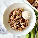 A healthy apple crisp topped with a scoop of vanilla ice cream in a bowl next to a napkin and spoon.