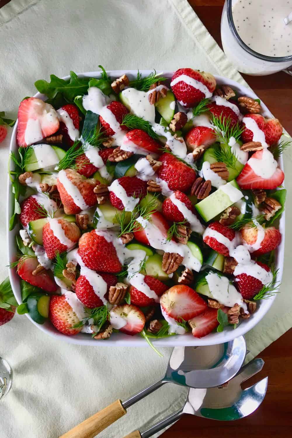 Strawberry Cucumber Salad with pecans and fresh dill in a square bowl, drizzled with a creamy dressing.